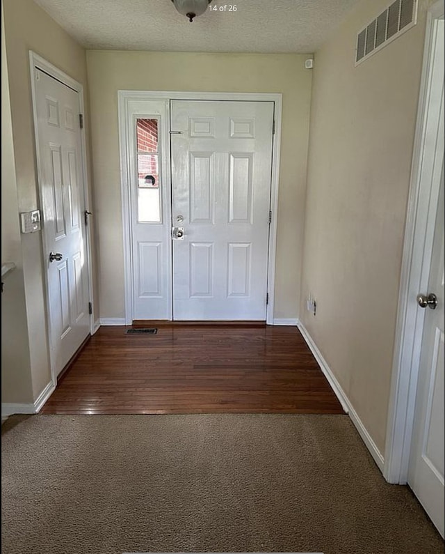 carpeted foyer entrance with visible vents, baseboards, a textured ceiling, and wood finished floors