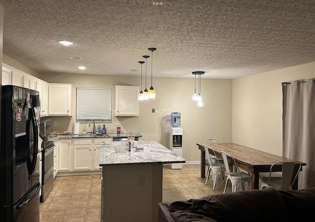 kitchen featuring gas stove, light stone countertops, black fridge, and white cabinetry