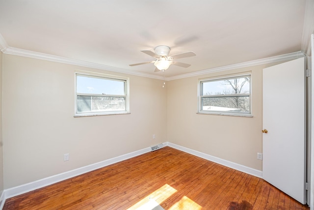 empty room featuring a wealth of natural light, crown molding, baseboards, and hardwood / wood-style floors