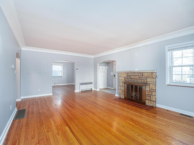 unfurnished living room featuring wood finished floors, visible vents, radiator heating unit, a fireplace, and arched walkways