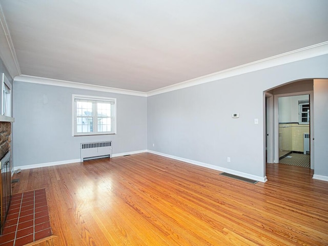 unfurnished living room with arched walkways, radiator, a stone fireplace, light wood finished floors, and baseboards