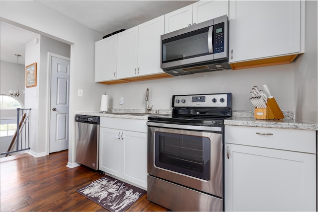 kitchen featuring light stone countertops, dark wood-style flooring, a sink, appliances with stainless steel finishes, and white cabinetry