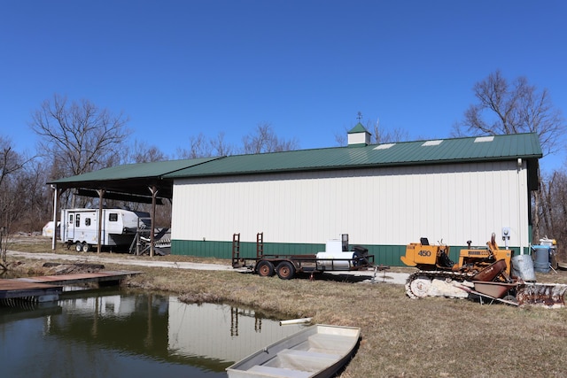 rear view of property with metal roof, a carport, an outdoor structure, and a pole building