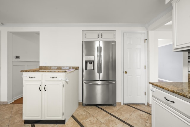 kitchen with ornamental molding, dark stone countertops, stainless steel fridge, white cabinets, and light tile patterned floors