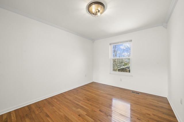 empty room featuring hardwood / wood-style floors, baseboards, and ornamental molding