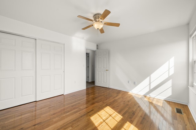 unfurnished bedroom with hardwood / wood-style flooring, baseboards, visible vents, and a closet