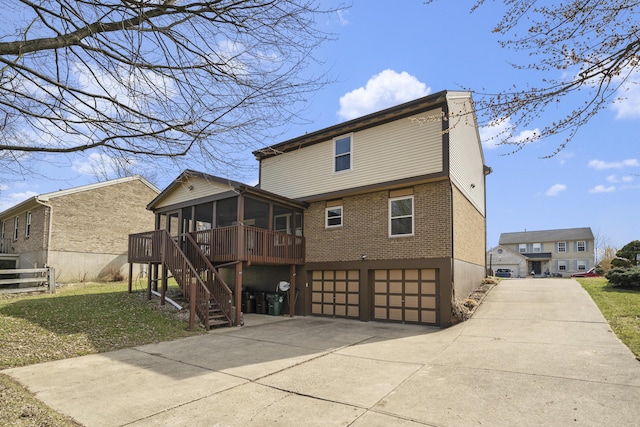 rear view of house featuring concrete driveway, stairway, a garage, and a sunroom