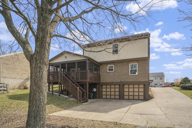 back of house with driveway, stairway, a sunroom, a garage, and brick siding