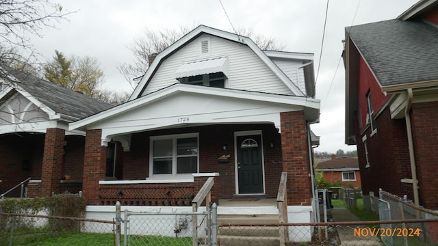 view of front of home with a gate, a porch, a gambrel roof, a fenced front yard, and brick siding