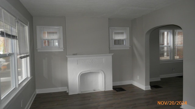 unfurnished living room with visible vents, baseboards, dark wood-type flooring, and arched walkways