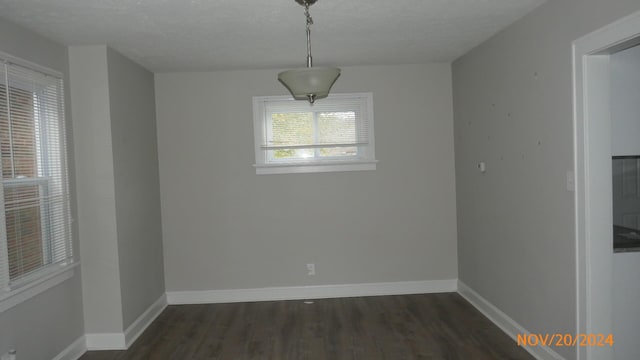 unfurnished dining area featuring a textured ceiling, dark wood-type flooring, and baseboards