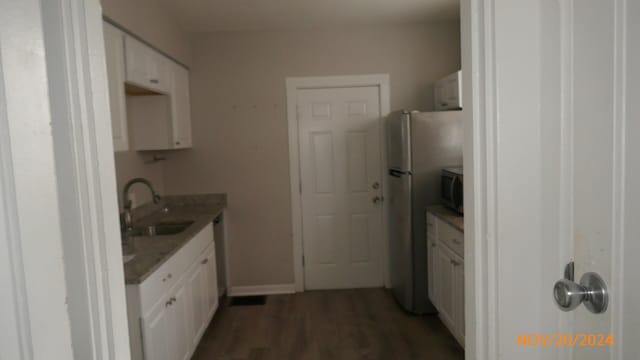 kitchen featuring wood finished floors, baseboards, a sink, appliances with stainless steel finishes, and white cabinetry