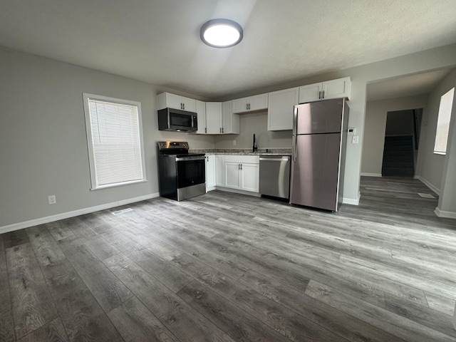 kitchen featuring wood finished floors, baseboards, white cabinets, and appliances with stainless steel finishes