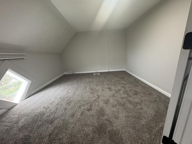 additional living space featuring baseboards, dark colored carpet, visible vents, and vaulted ceiling