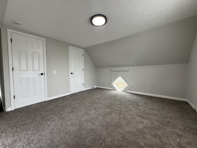 bonus room featuring lofted ceiling, a textured ceiling, baseboards, and dark carpet