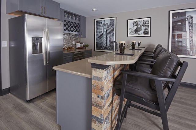 bar with beverage cooler, indoor wet bar, dark wood-type flooring, stainless steel refrigerator with ice dispenser, and backsplash