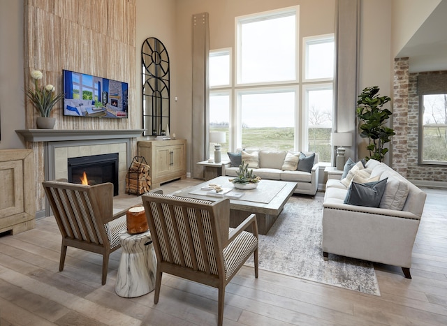 living room featuring a wealth of natural light, a fireplace, light wood-style floors, and a towering ceiling