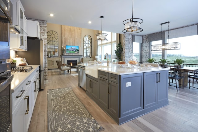 kitchen with stainless steel appliances, a sink, light countertops, white cabinets, and a large fireplace