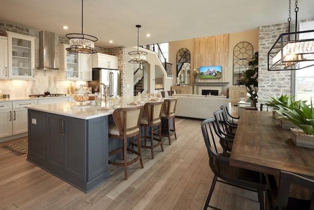 kitchen featuring an island with sink, light countertops, appliances with stainless steel finishes, a fireplace, and wall chimney exhaust hood