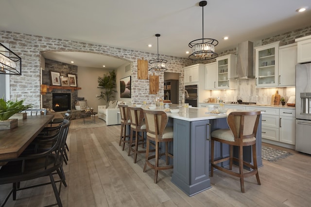 kitchen with light wood-style flooring, a fireplace, stainless steel appliances, white cabinets, and wall chimney range hood