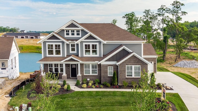 craftsman house with a water view, a front lawn, board and batten siding, a shingled roof, and brick siding