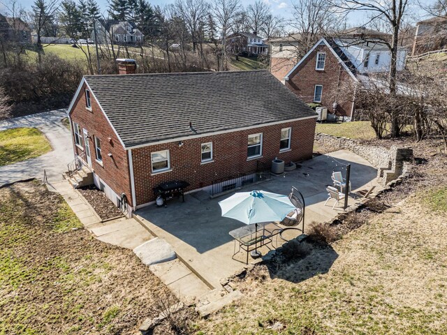 back of property featuring a patio, cooling unit, roof with shingles, a chimney, and brick siding