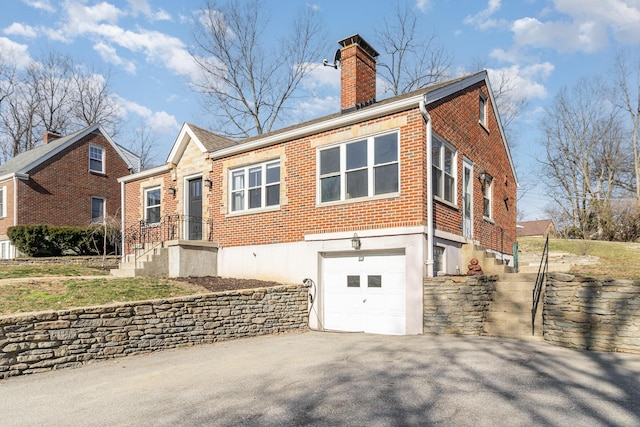 back of property with driveway, brick siding, an attached garage, and a chimney