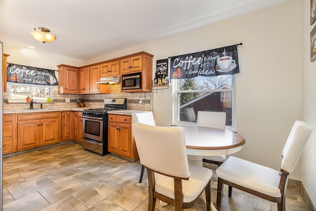 kitchen with brown cabinets, a sink, under cabinet range hood, appliances with stainless steel finishes, and decorative backsplash