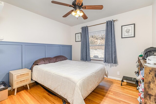 bedroom with a ceiling fan, wood finished floors, and wainscoting