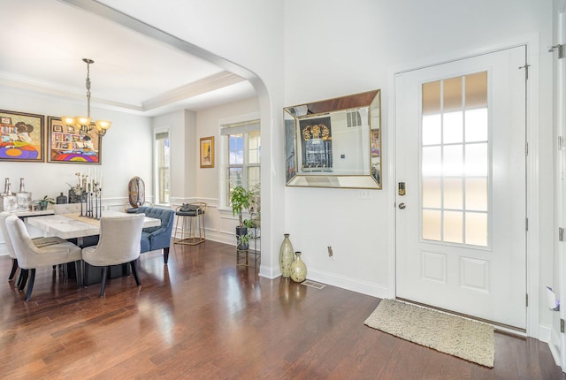 dining space with crown molding, a tray ceiling, wood finished floors, arched walkways, and a notable chandelier