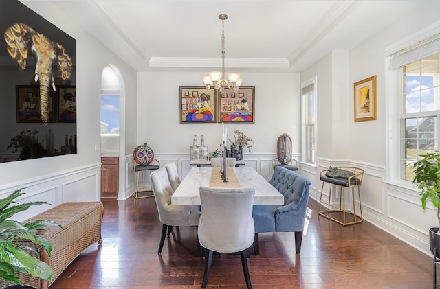 dining space with dark wood-style floors, a wainscoted wall, an inviting chandelier, a tray ceiling, and ornamental molding