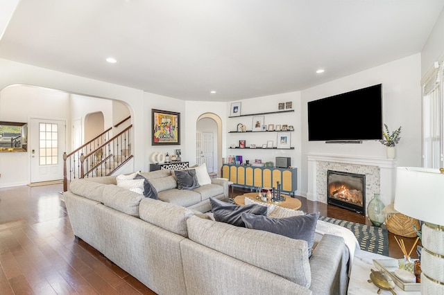 living area with stairs, recessed lighting, wood finished floors, arched walkways, and a glass covered fireplace