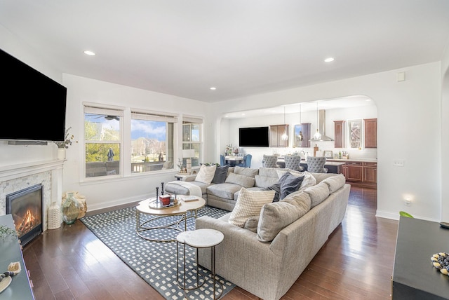 living room featuring arched walkways, a glass covered fireplace, dark wood-type flooring, and baseboards