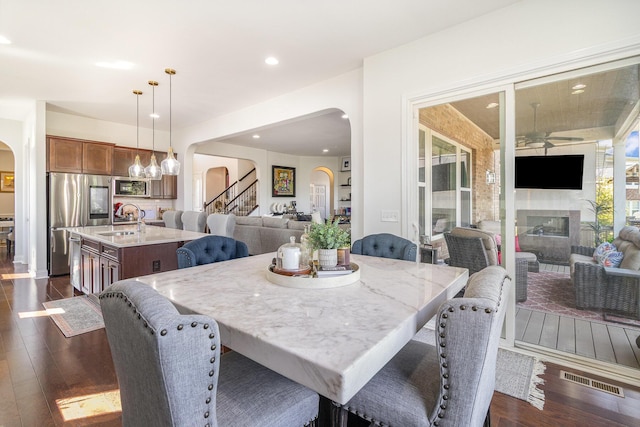 dining space featuring stairs, a glass covered fireplace, dark wood-style floors, and arched walkways