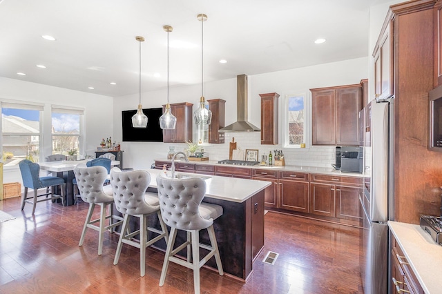 kitchen featuring visible vents, a breakfast bar, stainless steel appliances, light countertops, and wall chimney range hood