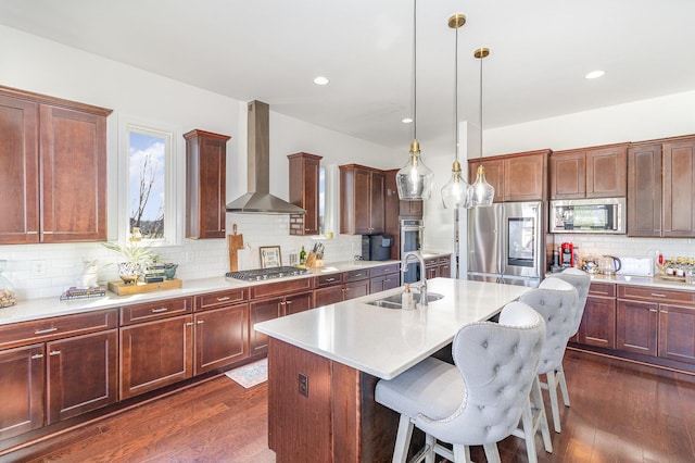 kitchen with appliances with stainless steel finishes, dark wood-type flooring, wall chimney range hood, and a sink