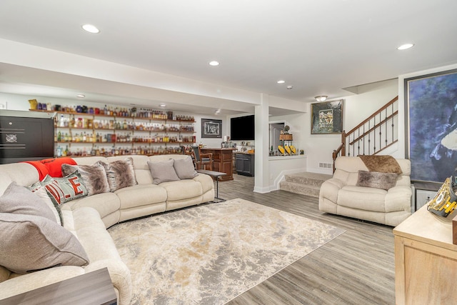 living area featuring recessed lighting, indoor bar, light wood-style flooring, and stairs