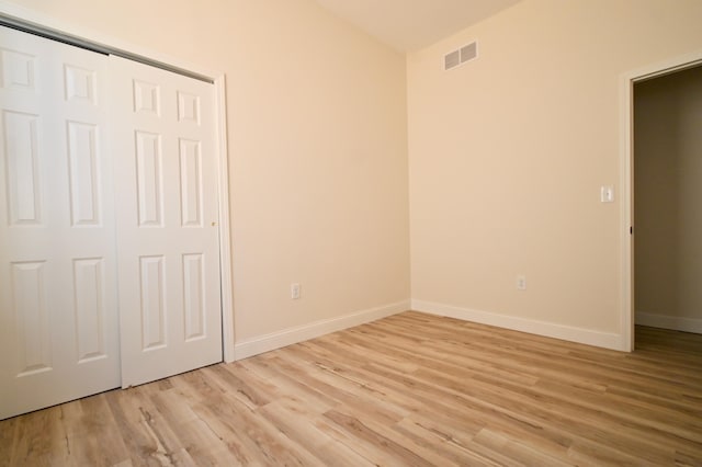 unfurnished bedroom featuring light wood-style flooring, baseboards, visible vents, and a closet