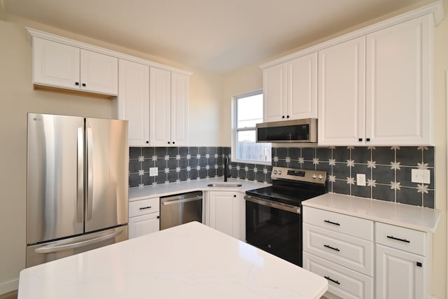 kitchen with a sink, tasteful backsplash, appliances with stainless steel finishes, white cabinets, and light countertops