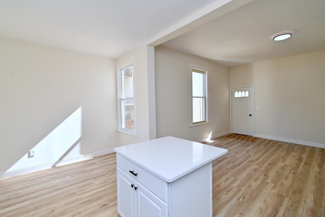 kitchen with light wood-style flooring, a kitchen island, white cabinetry, light countertops, and baseboards