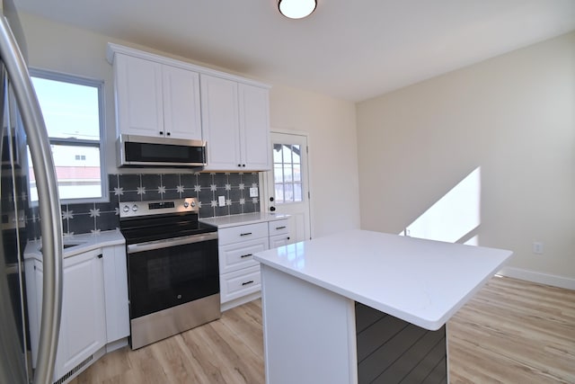 kitchen with light wood-type flooring, tasteful backsplash, white cabinetry, stainless steel appliances, and light countertops