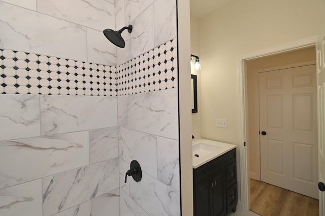 bathroom with a tile shower, vanity, and wood finished floors