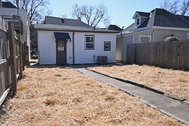 back of house with central AC unit, fence, and roof with shingles