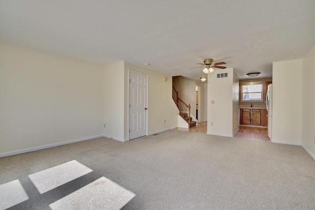 unfurnished room featuring visible vents, baseboards, stairway, light carpet, and a ceiling fan