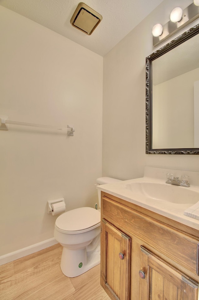 bathroom with toilet, a textured ceiling, wood finished floors, baseboards, and vanity