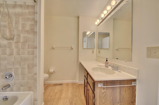 full bath featuring visible vents, toilet, wood finished floors, washtub / shower combination, and vanity