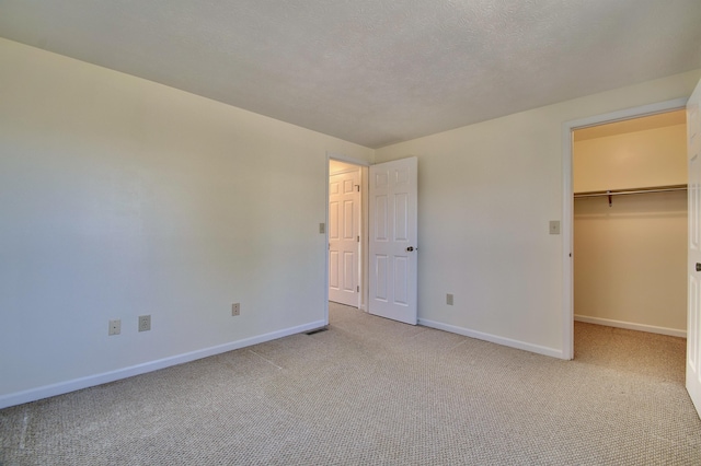 unfurnished bedroom with a spacious closet, light colored carpet, a textured ceiling, and baseboards