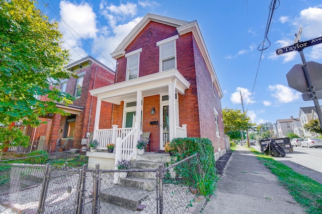 traditional-style house with brick siding, a porch, a fenced front yard, and a gate