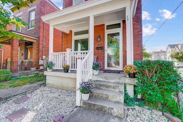 view of exterior entry with brick siding and covered porch