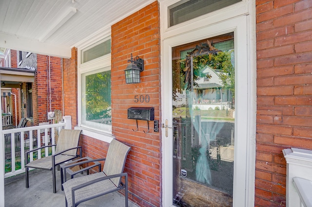 view of exterior entry with a porch and brick siding